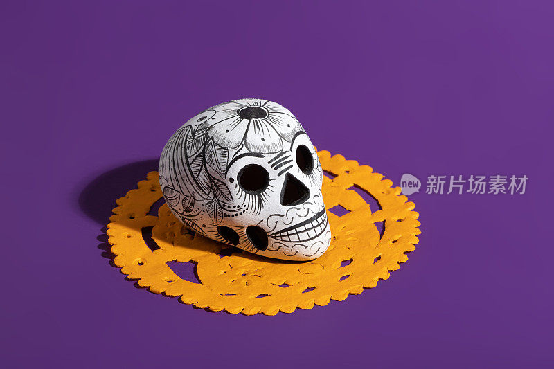 死亡之日的陶器头骨(calavera)在橙色papel picado在紫色背景，Dia de Muertos背景